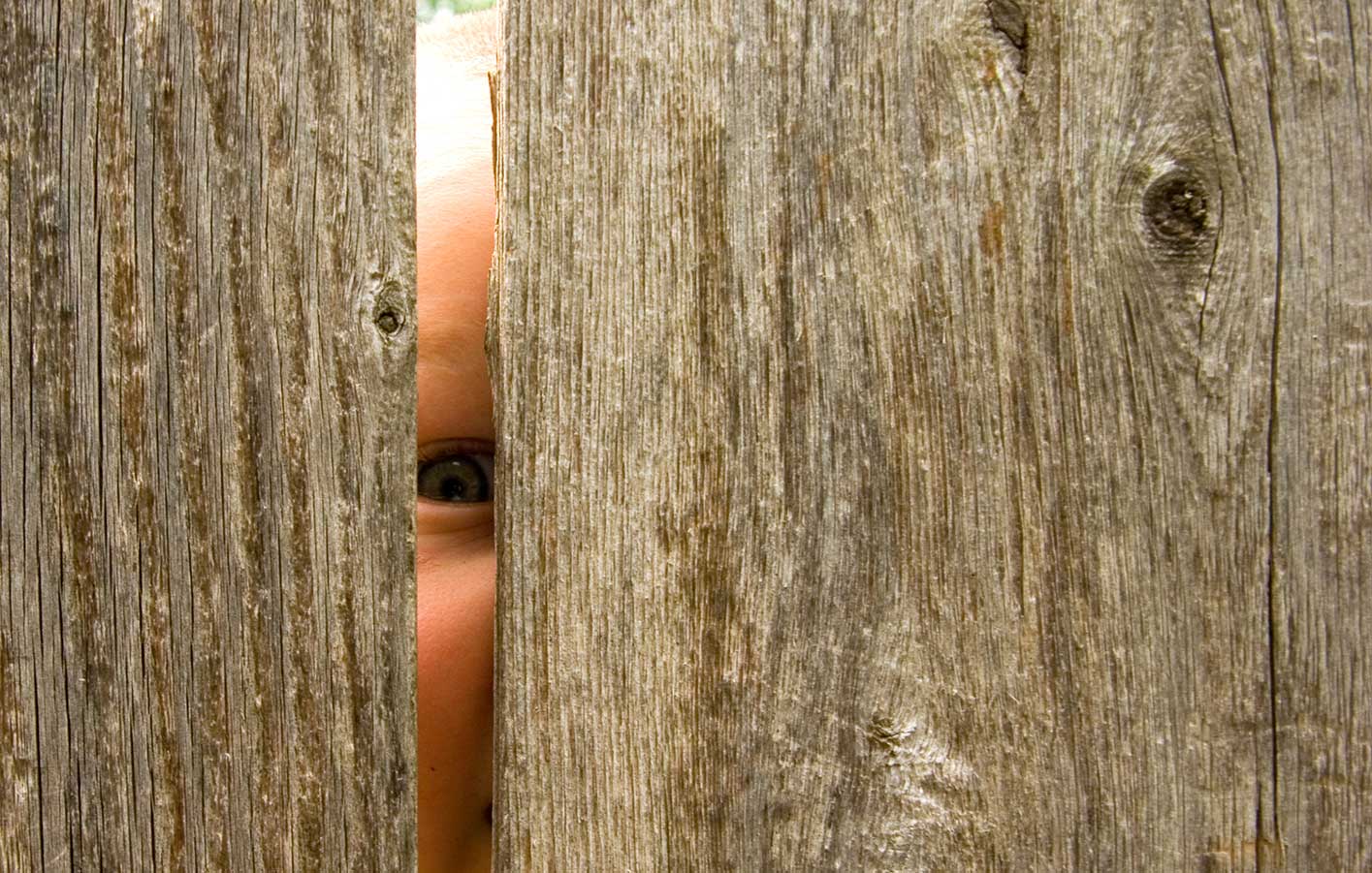 Neugieriges Kind schaut durch einen Sichtschutzzaun aus Holz